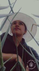 Imagen inspiradora de una joven líder rural entre hojas verdes, con sombrero blanco que simboliza trabajo y protección. Ideal para contenidos sobre empoderamiento femenino, liderazgo agrícola y sostenibilidad en zonas rurales.
